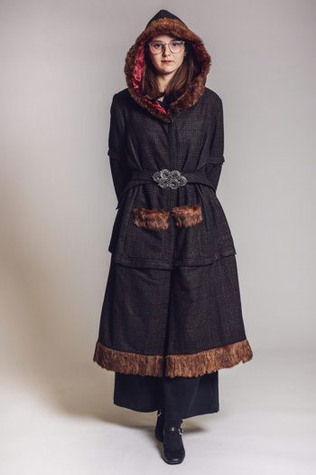 Model wearing a long, dark tweed coat with brown faux fur trim on the hood, pockets and hem, cinched at the waist with a matching fabric belt with ornate silver buckle.