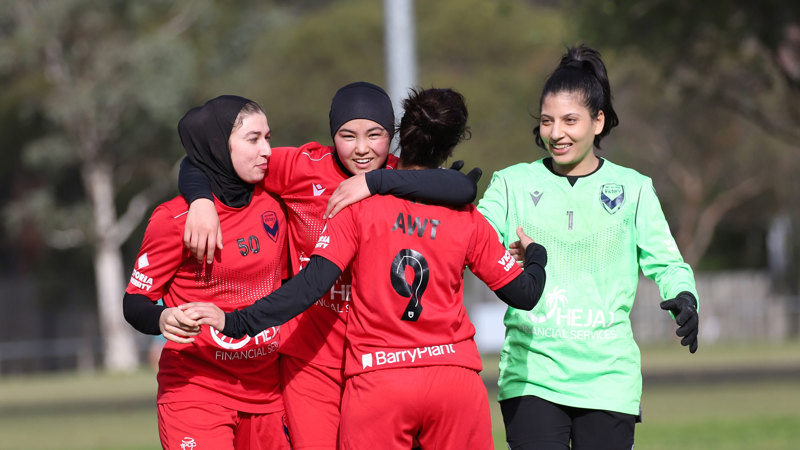 Members of the Afghan Women’s celebrating a goal on the field with smiles and hugs.