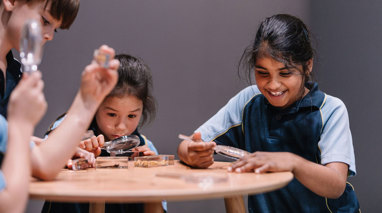 Four students around a small table, the students are really excited and curious as they look at insects through hand lens.