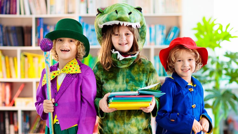 Three children dressed up, boy as Willy wonka, girl as T. Rex and small boy in Paddington Bear outfit, blue jacket and red hat.