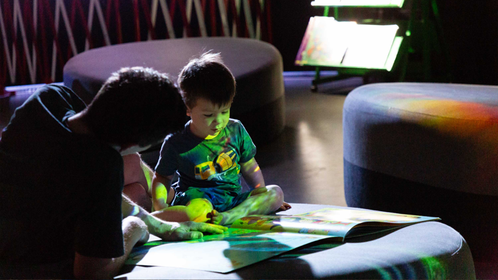 Family reading a book at Book Nook display in the Beyond Perception exhibition, during the Little Kids Day In program at Scienceworks, on 8th December 2023.