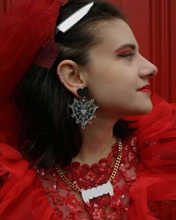 Woman with a knife in her hair wearing spider web earrings and a zombie fang necklace.