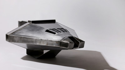 Metal model of an angular space shuttle with faceted silver-toned surfaces and geometric windscreen openings, mounted on a display stand.