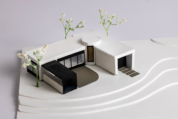 White architectural model of a modern, single-storey building with black floor-to-ceiling window frames.