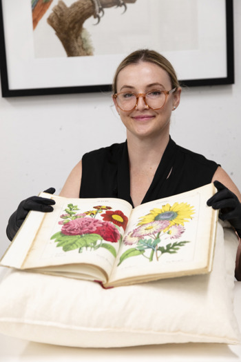 Shae Graham with a book that shows scientific illustrations of botanical specimens.
