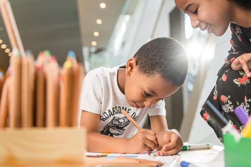 A child decorating and making a cardboard car while their sibling watches  