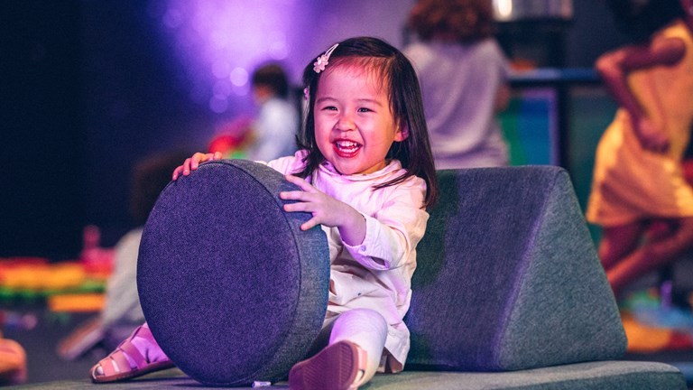 Child smiling and holding a round cushion.