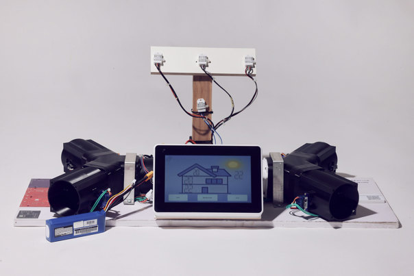 Prototype of a home automation system with a central touchscreen displaying a house schematic, with visible wiring and black plastic components.