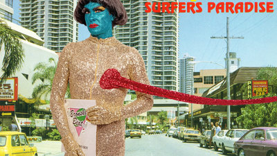 a person covered from head to toe in a glittery body suit and glam makeup holds a record. Behind them is a backdrop of a Surfers Paradise Street taken during the 80s.