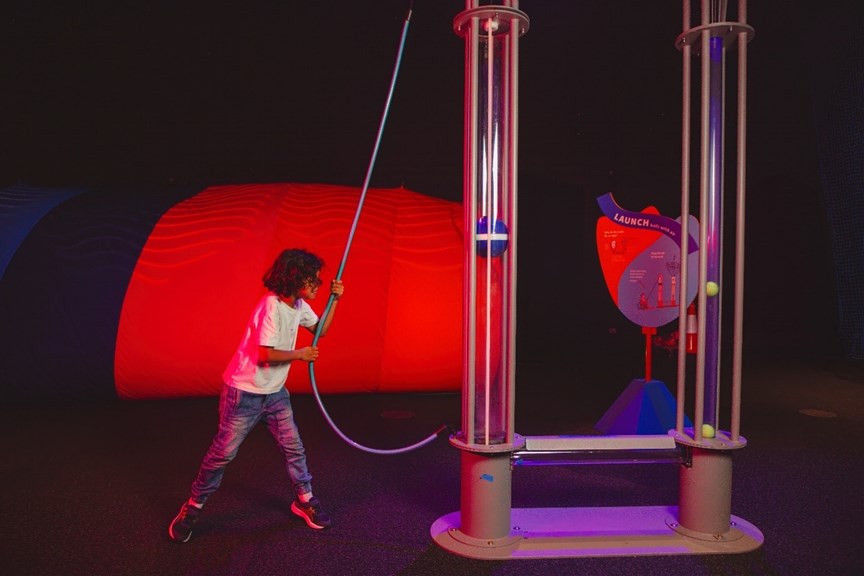 A boy pulling on a weight to activate exhibition interactive.