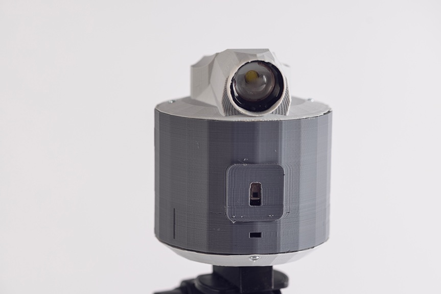 Grey cylindrical spotlight with a lens on top and a small control panel on the front.