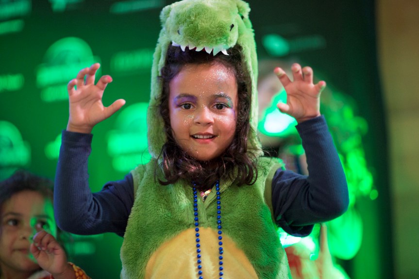 A child poses as T. rex in a dinosaur costume.