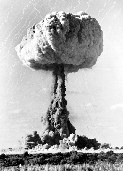 A black and white photo of a mushroom shaped cloud over a desert