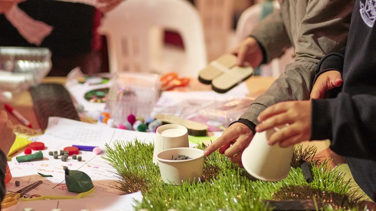 A table with craft materials and hands are visible putting things together.