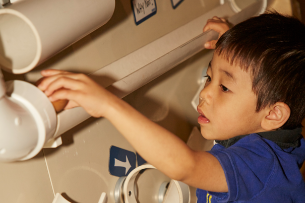 A child learning about gravity using a ball run made of pvc pipe at Scienceworks during Little Kids Day In.