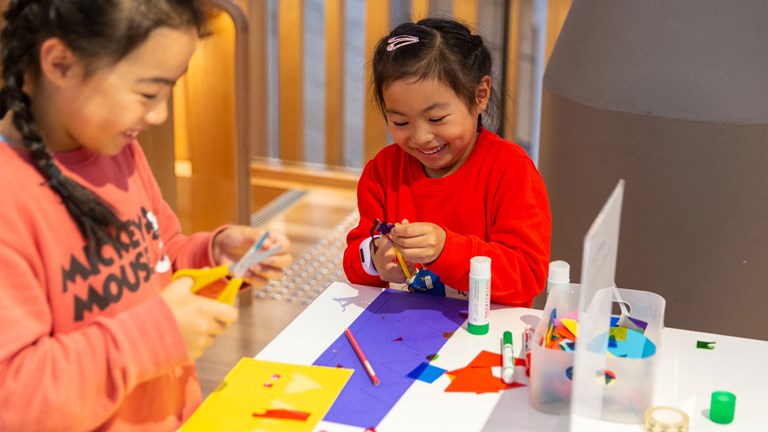 Two smiling children cut out coloured paper to make a book.
