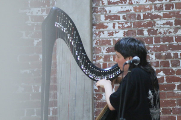 Genevieve Fry wearing black playing a black harp.
