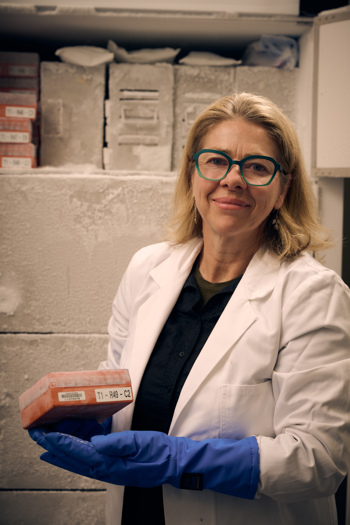 Dr Joanna Sumner holding orange box of frozen genetic materials in front of large freezer.