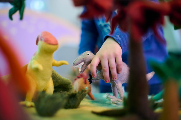 Children exploring dinosaur landscapes and open sensory play at a soft play station containing toy dinosaurs.