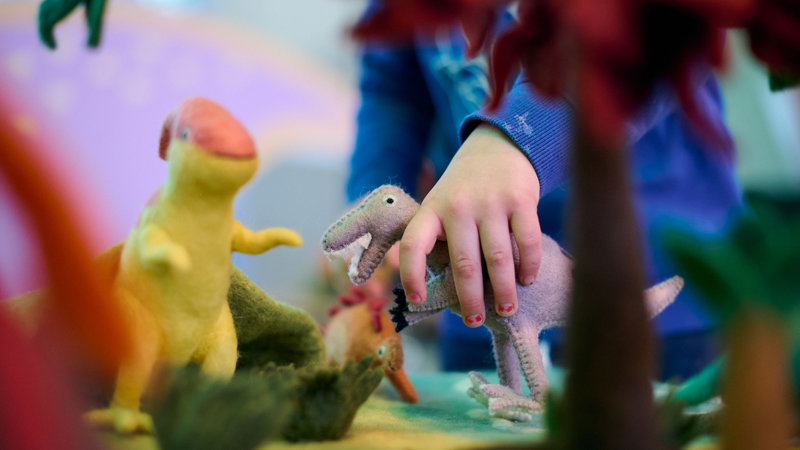 Children exploring dinosaur landscapes and open sensory play at a soft play station containing toy dinosaurs.