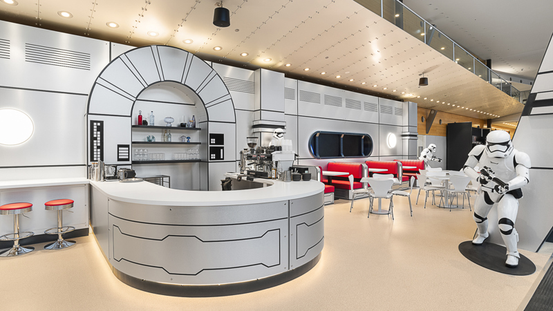 Interior view of the Galactic Café, styled like a Star Wars spaceship, with red booth seating, white tables, and Stormtrooper figures.