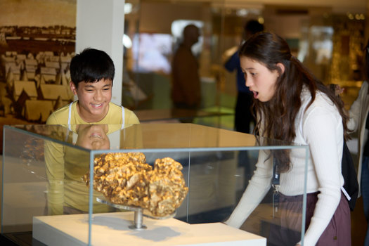Teenage siblings looking at a replica of a large gold nugget in a display case.