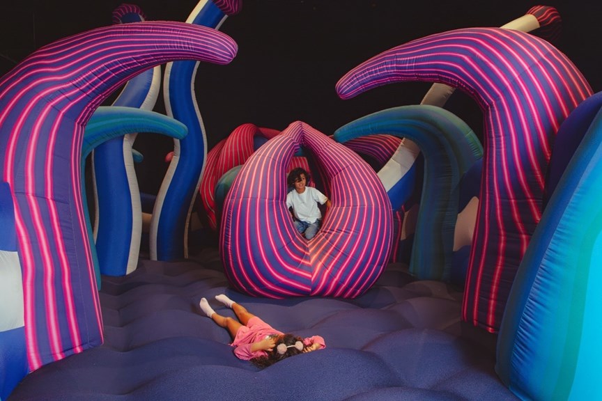 A child lying on a large air cushion which has pink and purple arms.