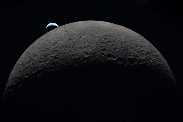 Image of the far side of the moon with a crescent earth partially visible in the background.