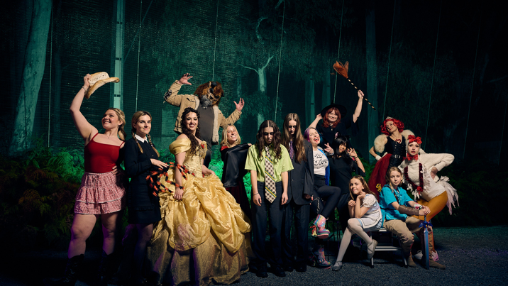 A group of people dressed up in assorted Halloween costumes pose in front of the formidable forest.
