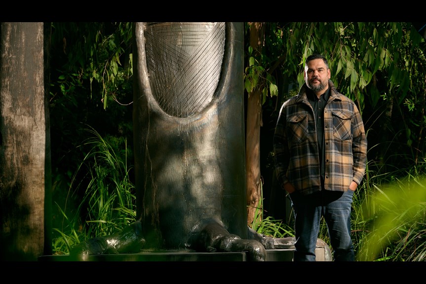 A man stands in front of a metal tree sculpture. 