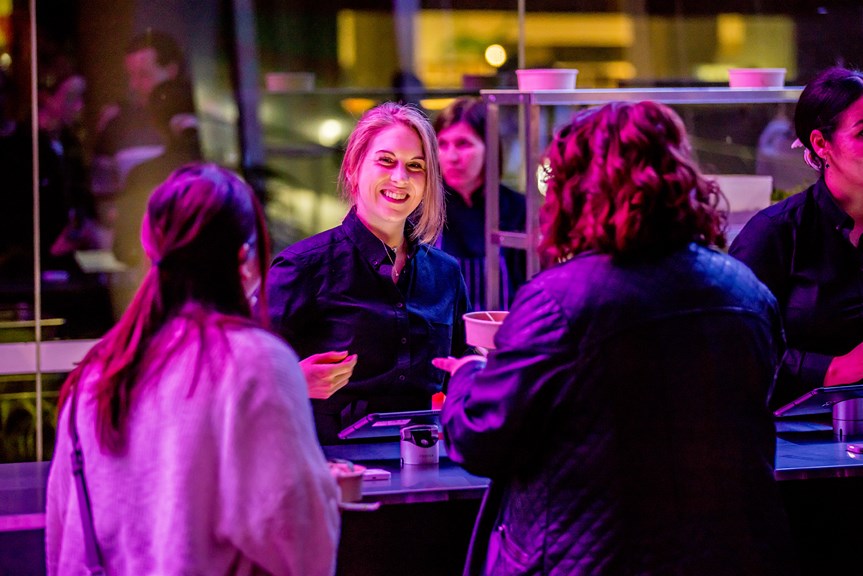 A woman smiles as she hands a order of food to museum goers.