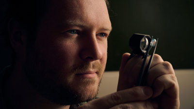 Researcher examining a small specimen through a magnifying lens while holding it with tweezers.