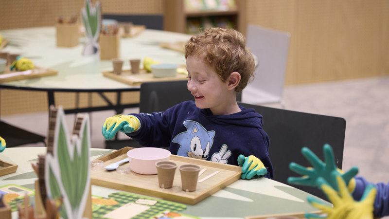A young boy wearing gloves potting seeds while taking part in the Seed Stories workshop at Melbourne Museum.