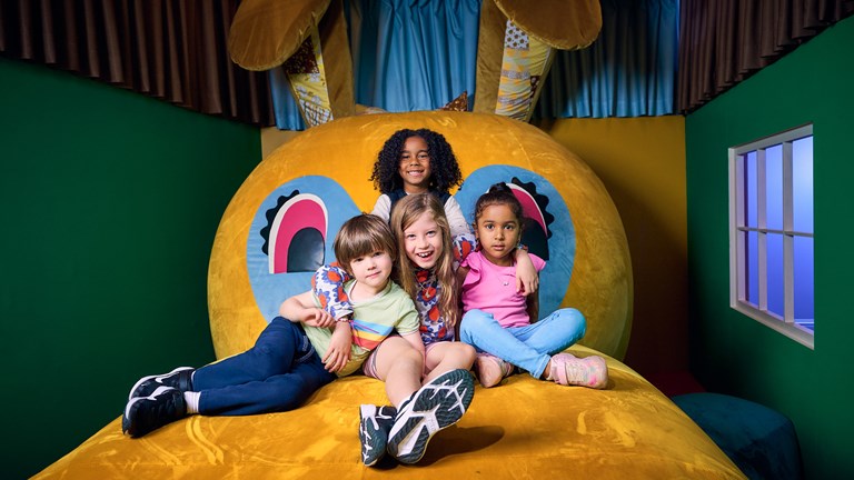 Four children with their arms around each other sit atop the belly of a reclined giant rabbit.