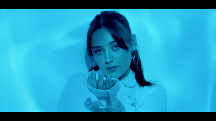 Blue toned image of a young person looking directly at the camera, holding up their hands.