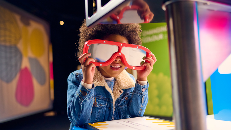 A child with large red glasses on in Colour exhibition at Scienceworks.