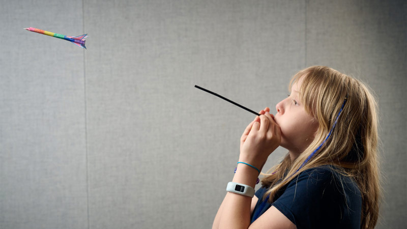  A child is blowing through a straw, which has pushed a small paper-rocket through the air. 