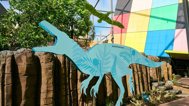 A blue silhouette of a Raptor-esque Australovenator dinosaur illustrated with plants standing in the Gandel Gondwana Gardens