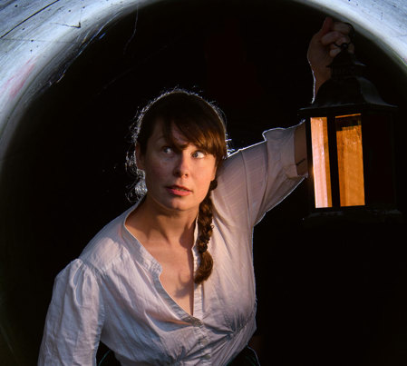Alanta Colley in a  white shirt carrying a hand-lamp through a dark tunnel