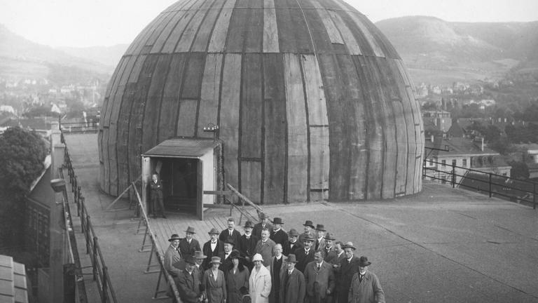 A large group of well-dressed people pose at the opening of the world’s very first opto-mechanical projection planetarium in 1923.