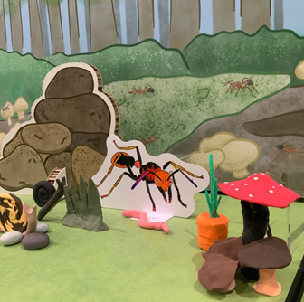 A ant and rock pile coloured illustration sits next to a plasticine mushrooms and carrots in a close-up of a bugs themed Diorama.