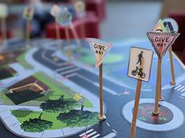 A selection of coloured in mini paper road signs on sticks have been placed on a vinyl road map with Blu Tack.