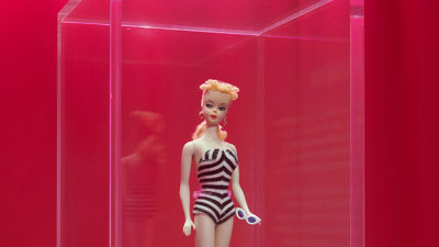 A Barbie wearing a black and white stripe shoulderless onesie holding sunglasses. The display reads: 'Barbie Doll, 1959'