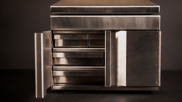 A stainless steel jewellery box with one of its doors open, revealing a series of small shelves inside.
