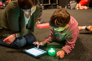 A child showing thier guardian how to use an iPad to control a sphero robot.