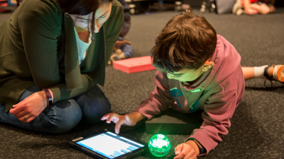 A child showing thier guardian how to use an iPad to control a sphero robot.